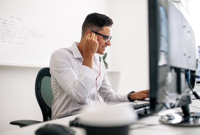 Man wearing spectacles on phone and working on laptop computer in office