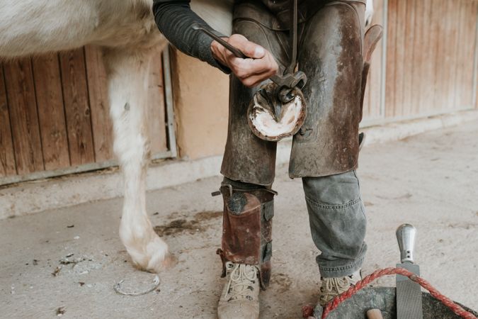 Man shoeing horse near stable