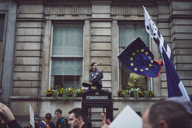 London, England, United Kingdom - March 23rd, 2019: Woman waving EU flag sitting atop a phone booth