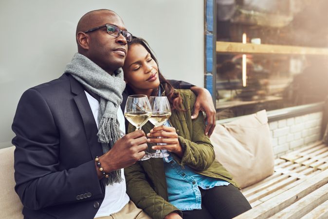 Black couple in each others arms while dining alfresco with wine in hand looking relaxed