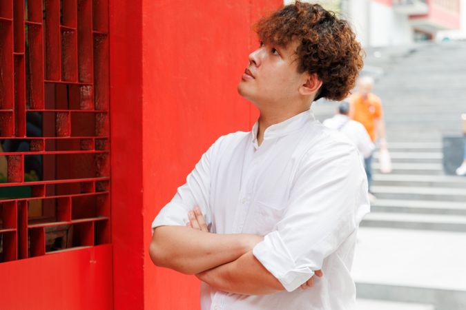 Portrait of Asian man in button up shirt standing with arms crossed by red building