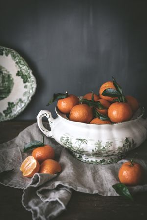 Orange tangerines in ceramic ornamental bowl on wooden table