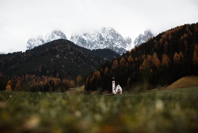 Small church on cliff near forest and mountains