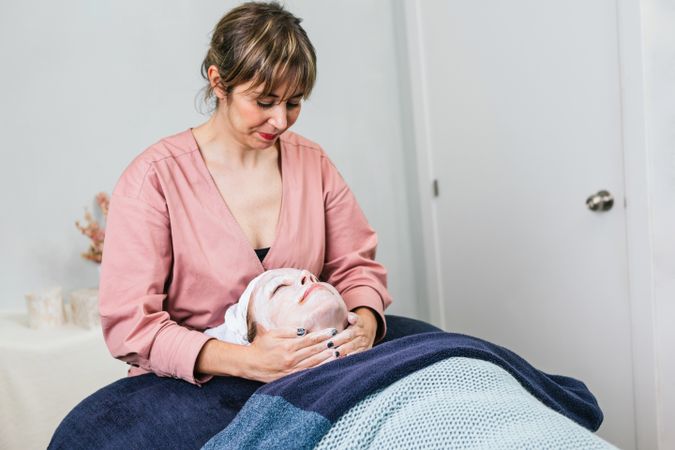 Crop beautician cleansing face of woman in salon