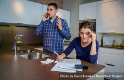 Man making phone call as woman works on bills in kitchen counter 5rRq25