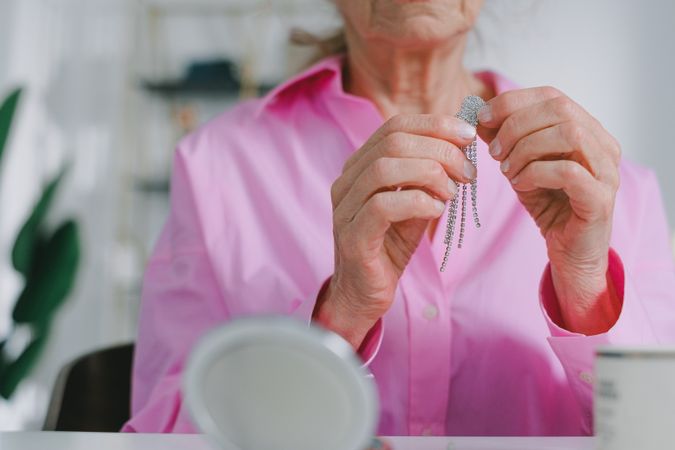 Older woman in pink button up shirt holding a diamond earring