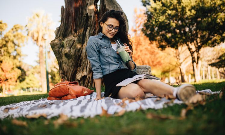 Beautiful young woman sitting at park drinking juice and reading an interesting book