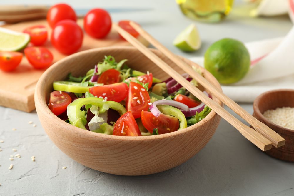 Fresh salad with chopsticks and kitchen accessories on grey background, close up
