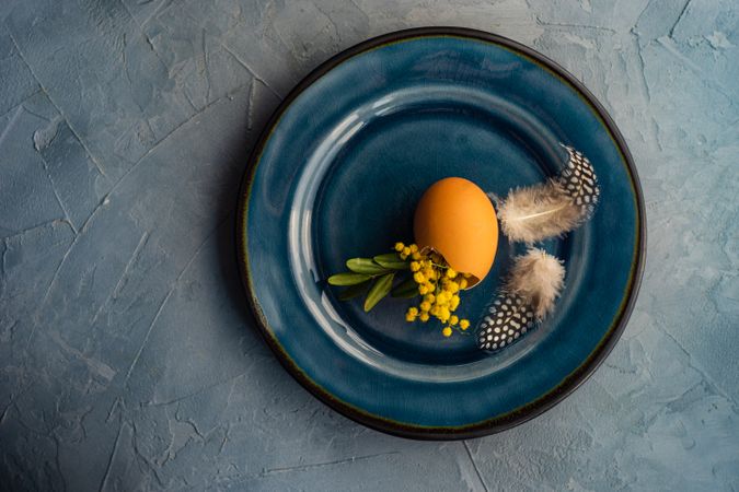 Top view of Easter table setting with egg and feather on blue plate
