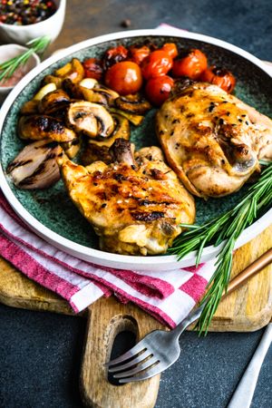 Plate of grilled chicken with tomatoes and mushroom on counter