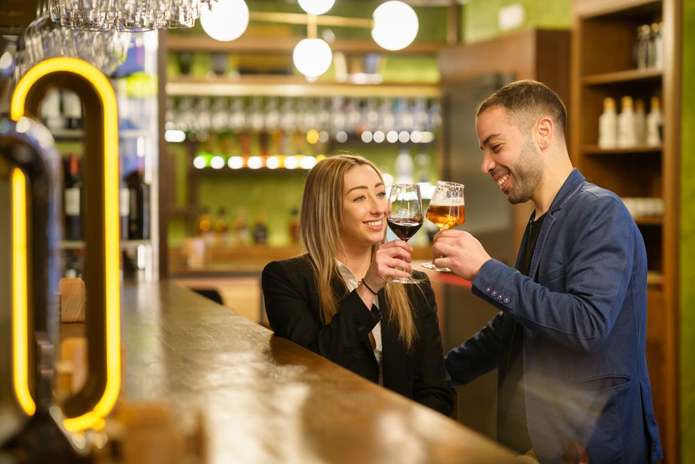 Happy man and woman toasting beer and wine at a bar or lounge