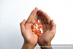 Two hands holding variety of colorful medication and vitamins with plain background 47mX8B