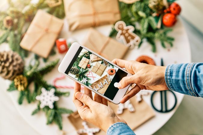 Faceless person with phone photographing Christmas gifts