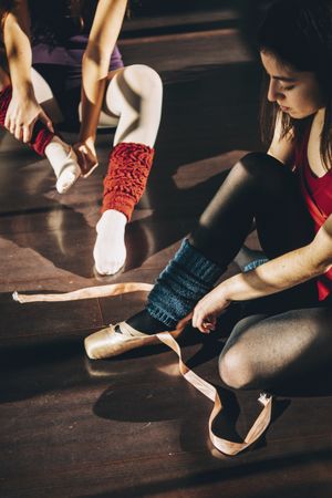 Young ballerinas wearing and lacing white pointe shoes in studio.
