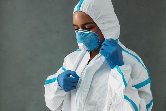 Black woman adjusting her hazmat suit in protective gloves and face mask