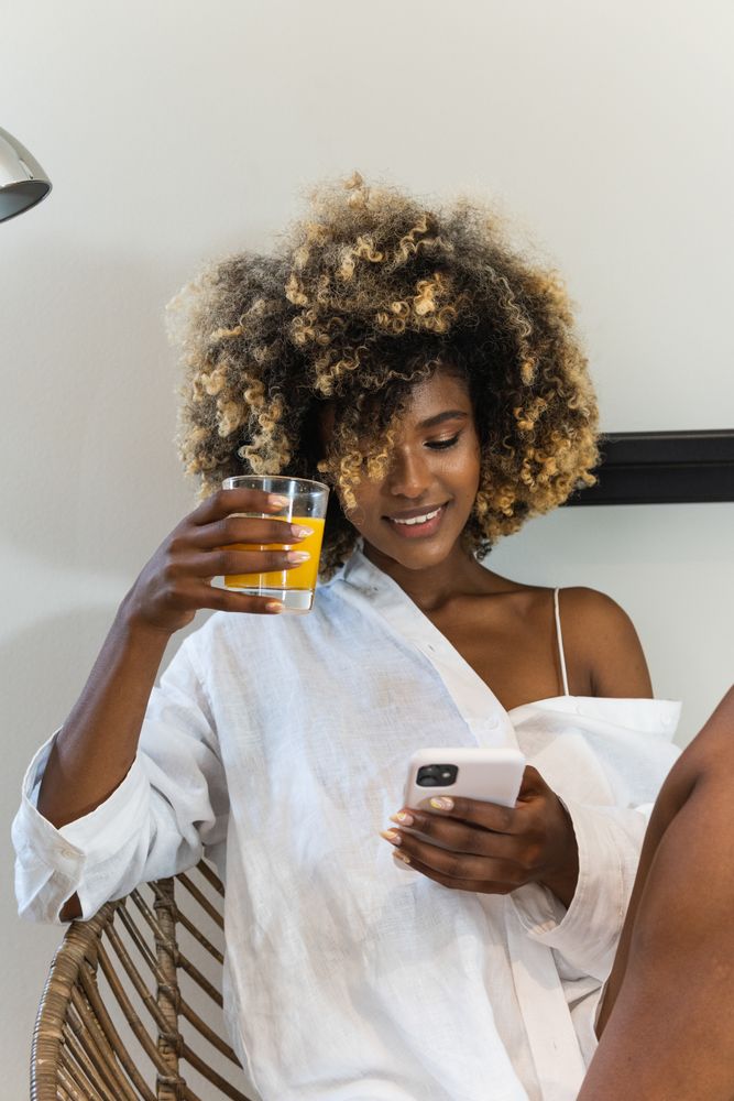 Happy Black woman sitting on armchair surfing smartphone