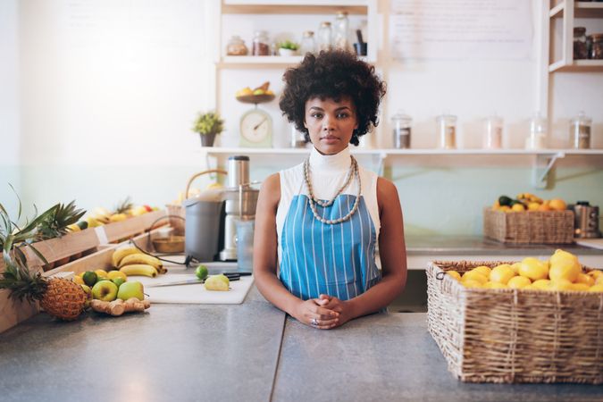 Portrait of young woman wearing apron standing behind juice bar