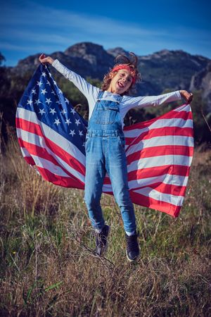 Happy preteen boy having fun with American flag in field