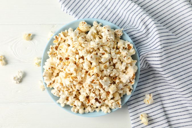 Flat lay composition. Towel and plate with popcorn on wood background