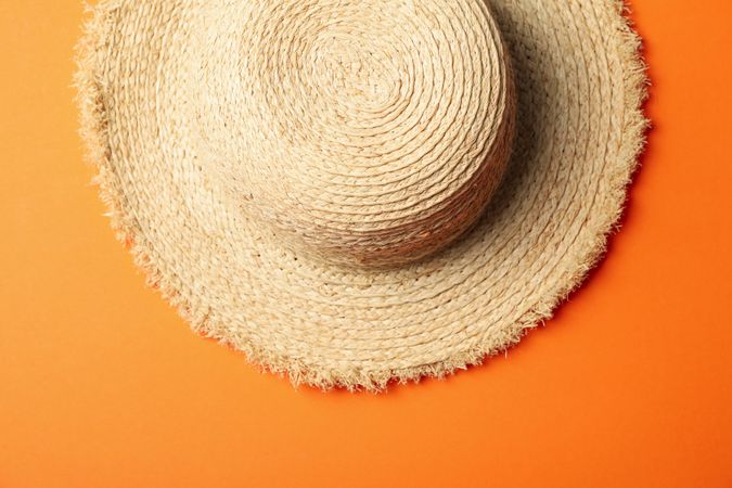 Straw hat on orange background, top view