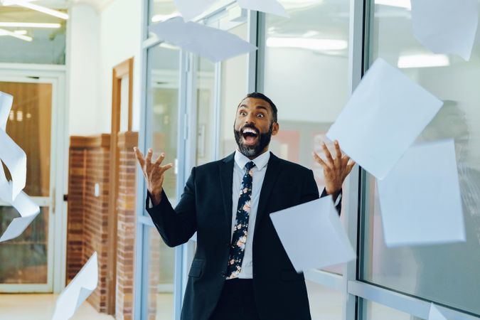 Delighted businessman in suit and tie throwing papers in the air in office