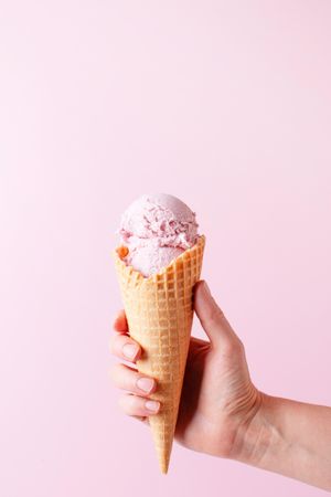 Woman’s hand holding pink ice cream in cone