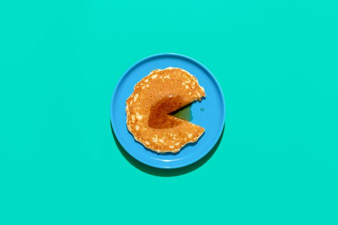 Top view of pancake topped with maple syrup on bright blue plate and green background