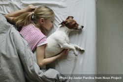 Top view of young girl sleeping  on bed with her arm around dog bE9aMb