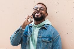 Cheerful Black man talking on phone near wall