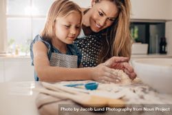 Little girl preparing dough on kitchen counter with her mother 56wae4