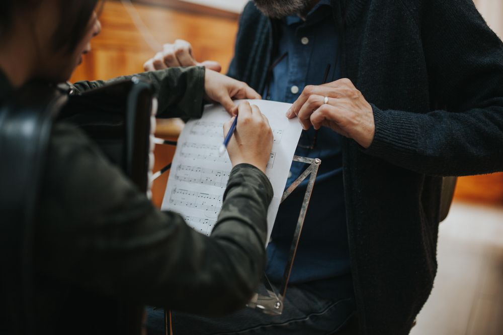Student using pencil to mark sheet music with teacher in front of her