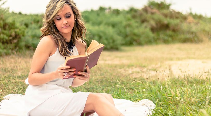 Romantic woman reading a book sitting outdoors