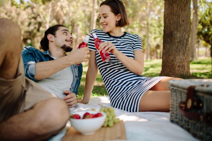 Cute couple toasting glass bottles at a picnic
