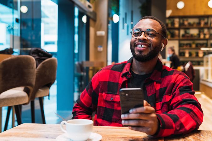 Cheerful Black man with smartphone in cafe