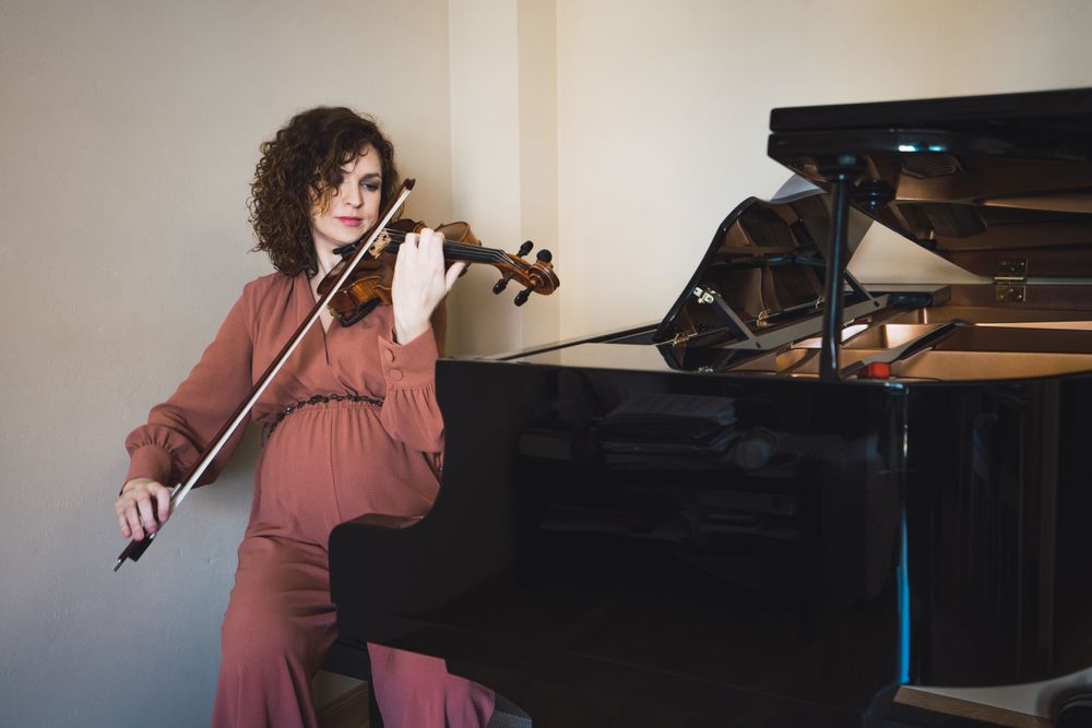 Pregnant woman playing on violin near piano in room