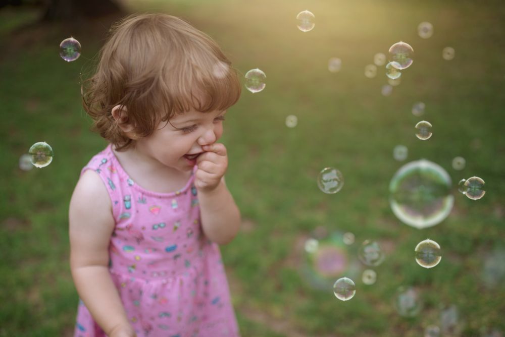 Joyful girl playing with colorful bubbles in grass