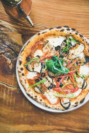Wood fired vegetable pizza on wooden table with olive oil