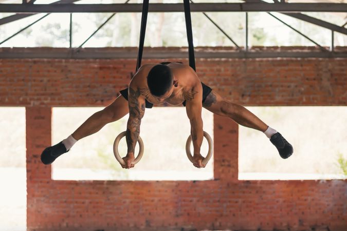 man athlete training in gymnastic rings doing a straddle planche