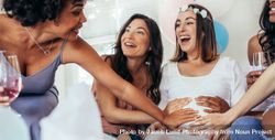 Friends touching pregnant woman's belly at baby shower party 0V6OQX