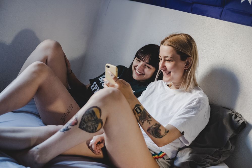 Happy lesbian couple using smartphone on bed