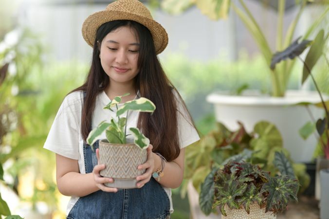 Asian female in a green house holding a plant