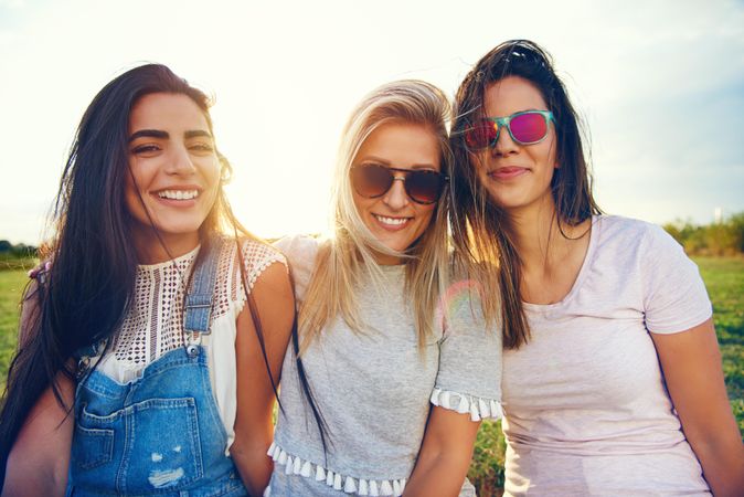 Happy multi-ethnic female friends sitting in sunny field looking at camera
