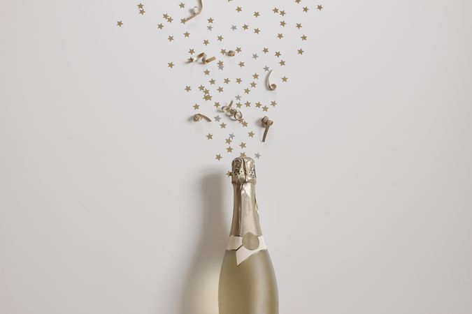 Happy new year still life bottle of champagne wine and star shape golden confetti on beige table background