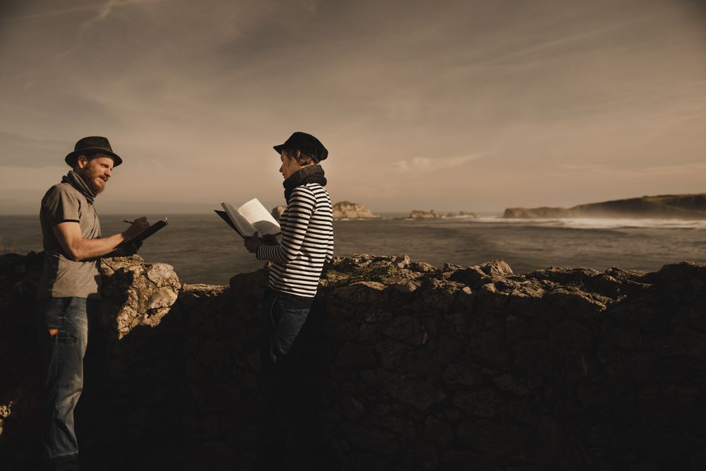 Man near woman with books near stones on shore