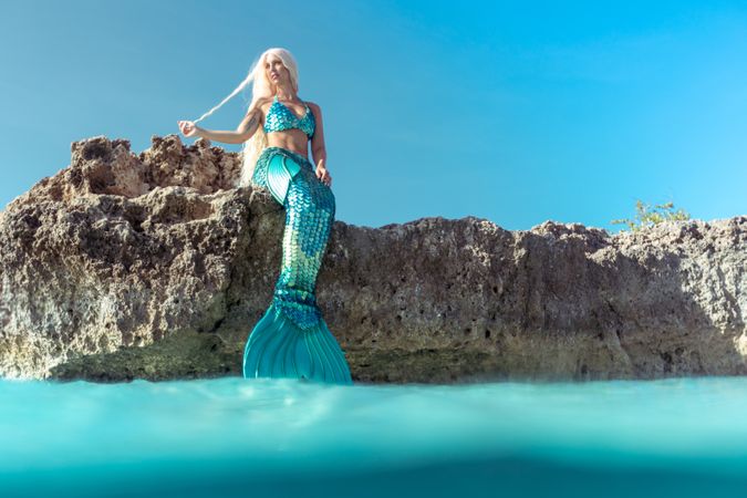 Blond fairytale female mermaid lying on rock