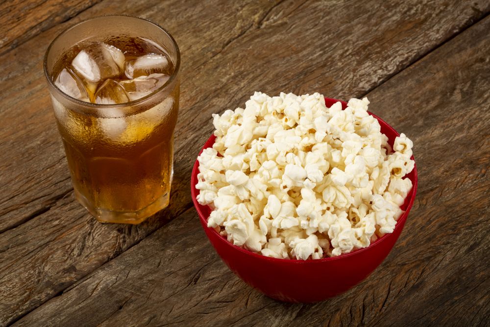 Bowl with salted popcorn and soda on the table.