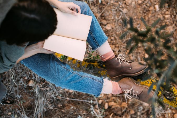 Above view of woman in jeans  and boots outdoors with book