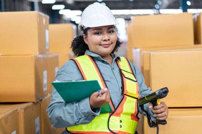 Woman in safety gear working in distribution center checking bar codes on inventory