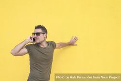 Serious male leaning on yellow wall talking on smartphone 56XZYb