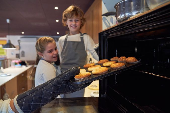 Faceless person taking cupcakes from oven near children